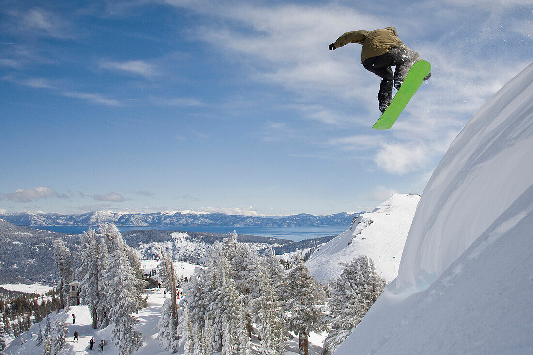 A snowboarder launching into fresh powder snow with mountains and blue sky in the background Squaw Valley, California, USA