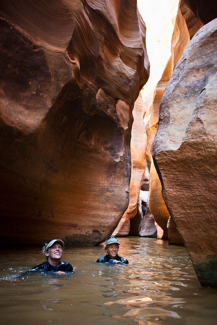 Two women wading through a deep pool in a slot canyon in Utah Utah, USA