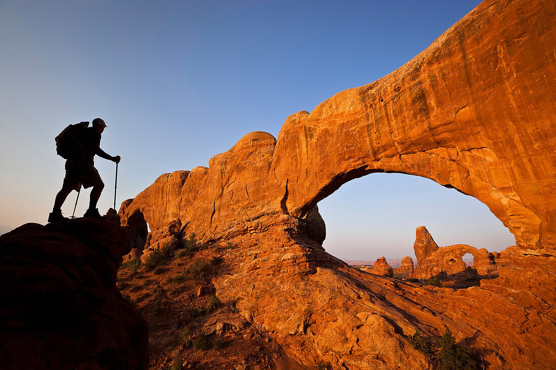 A silhouetted hiker stands looking at an arch in Arches National Park, Utah Moab, Utah, USA