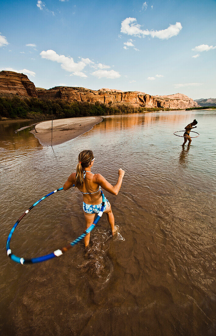 Two women playing and hula hooping in a shallow river Moab, Utah, USA