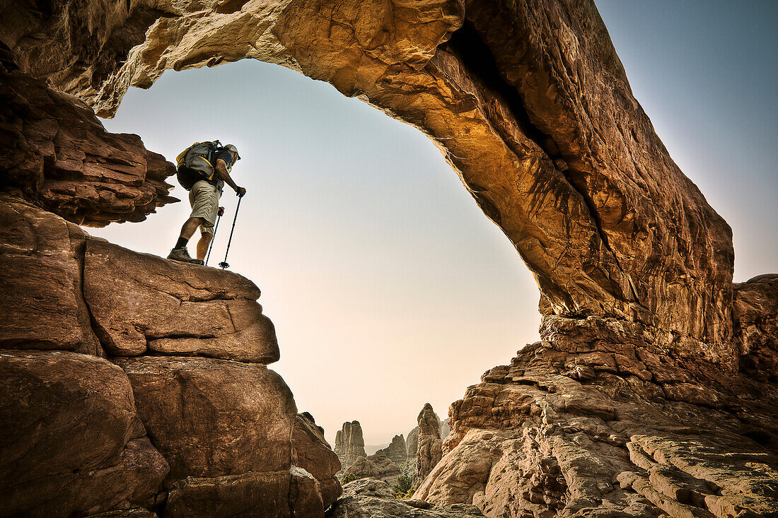 A hiker stands beneath an arch in Arches National Park, Utah Moab, Utah, USA