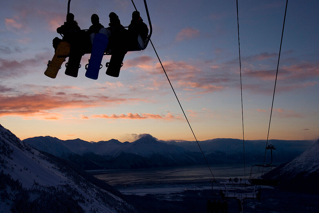 Four snowboarders are silhouetted on a ski lift at sunset Girdwood, Alaska, USA