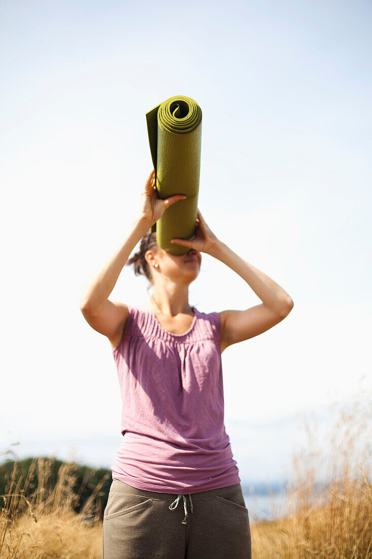 A young woman playfully looks through her yoga mat, acting like it is a telescope Seattle, Washington, USA