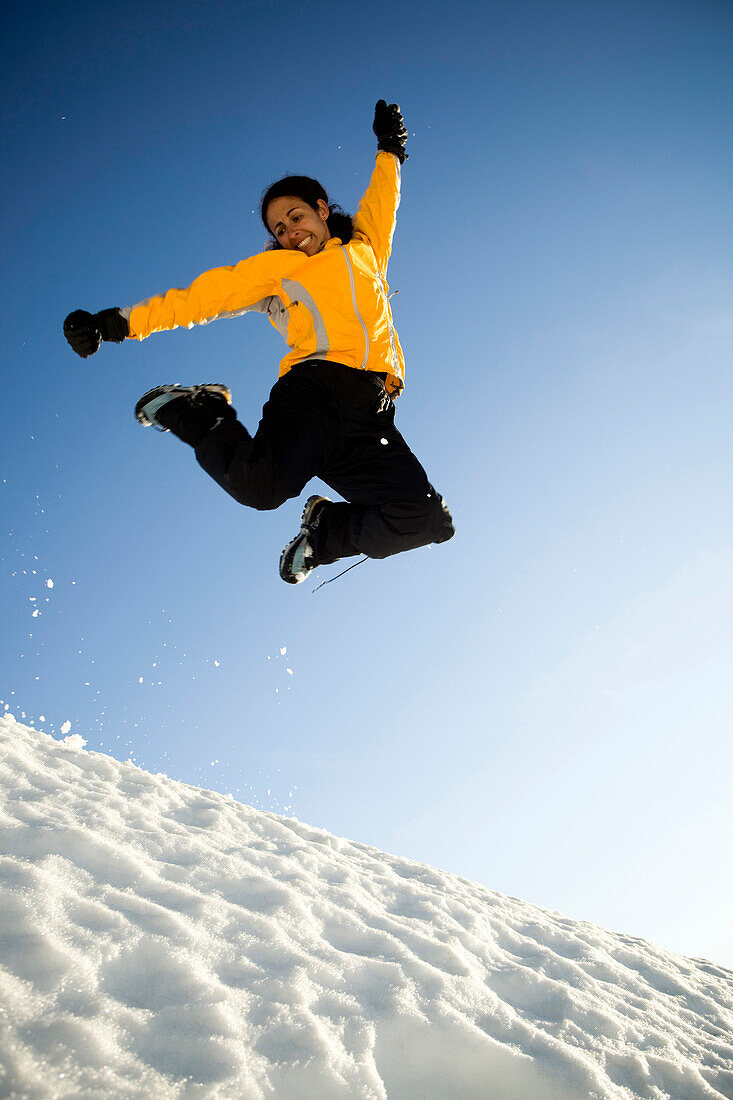 A Latina woman jumps in the sunny snow in the mountains North Cascades National Park, Washington, USA