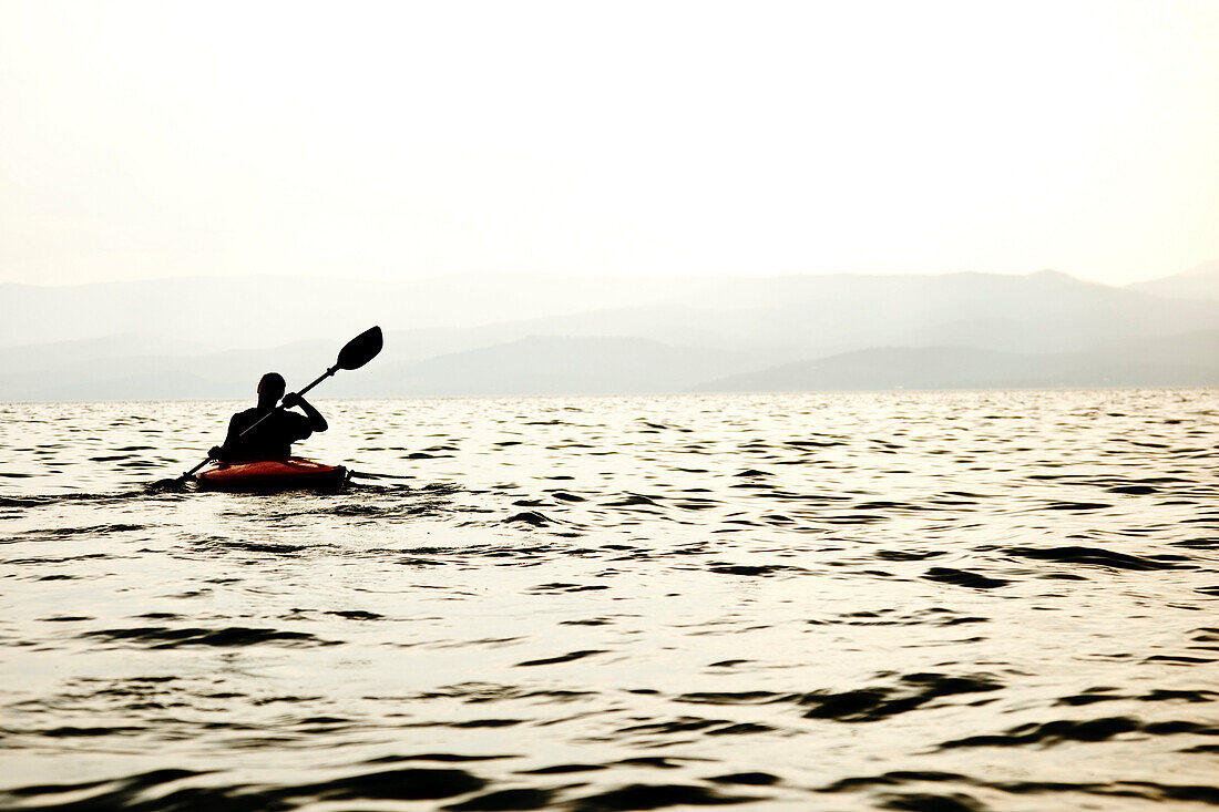 The silhouette of a male kayaker paddling across Flathead Lake, Montana, just before sunset Bigfork, Montana, USA