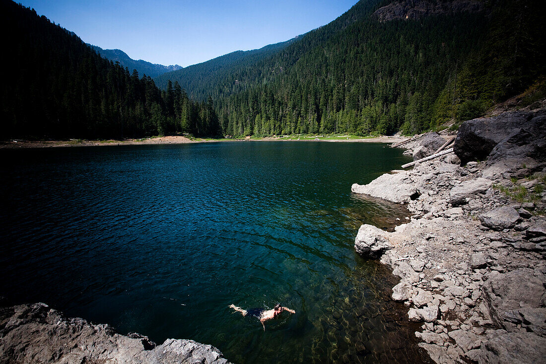 A young man swims in a high alpine lake on a sunny afternoon Washington, USA