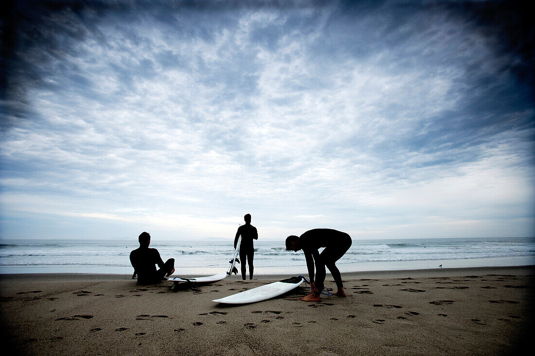 Three surfers on the beach getting ready to go surfing Ventura, California, USA