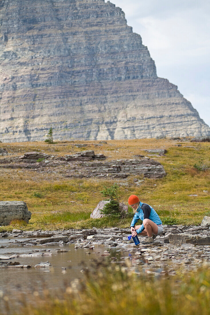 Solo female camper filtering water at an alpine lake Glacier National Park, Montana, USA