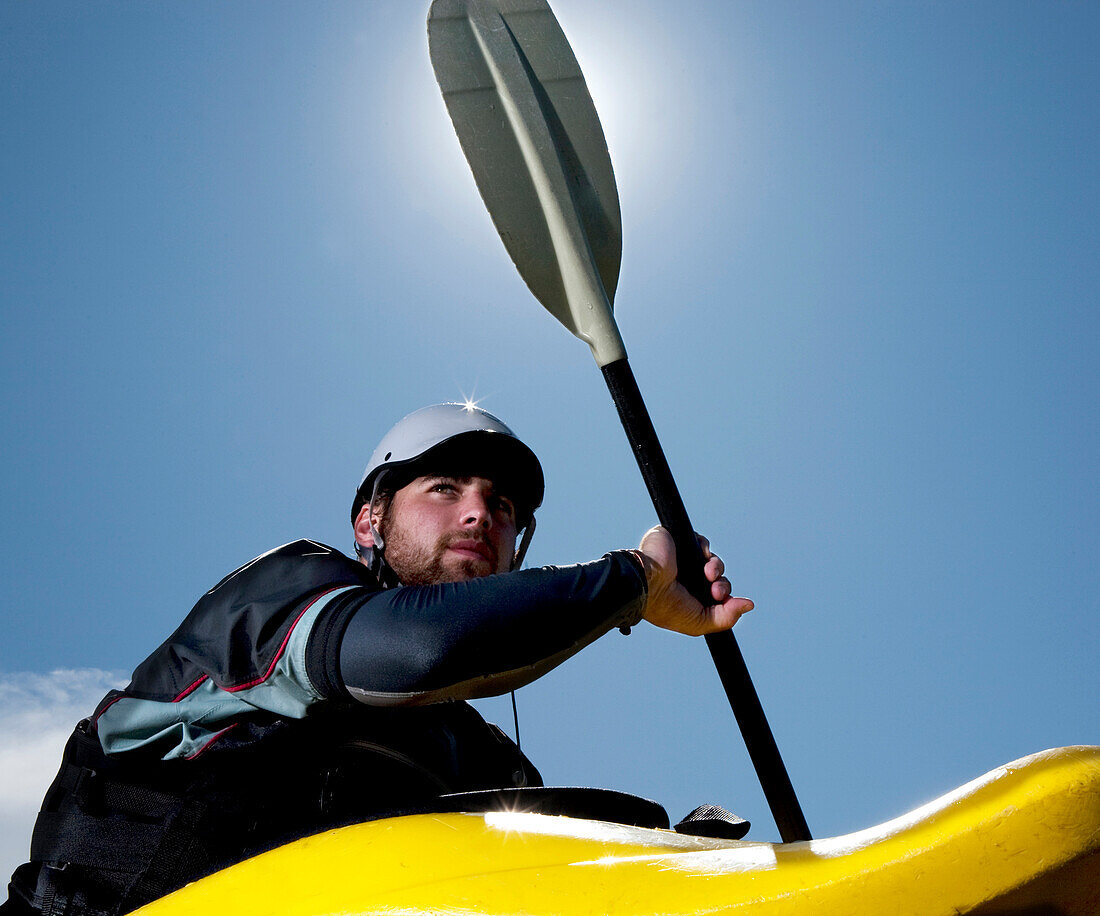 Low-angle view of a male kayaker in a playboat is backlit by the sun Missoula, Montana, USA