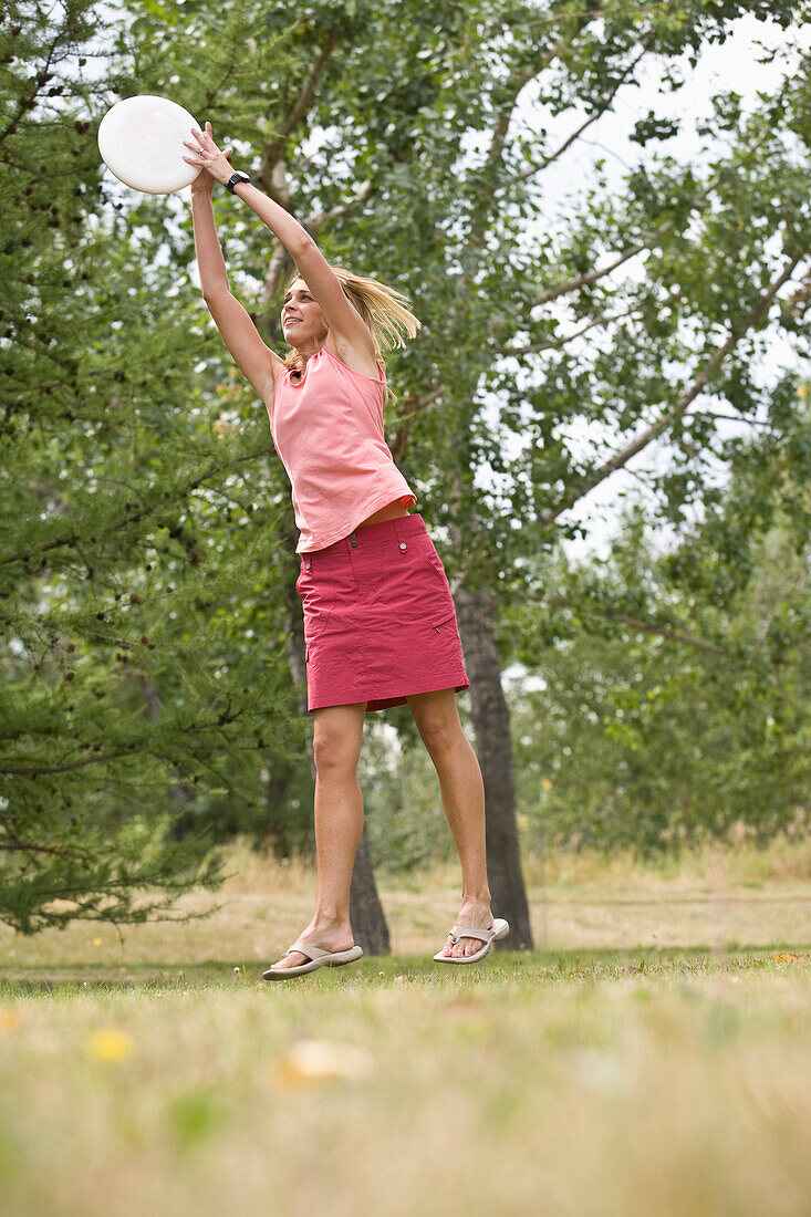 Woman going airborne to catch a frisbee in a green urban park Calgary, Alberta, Canada