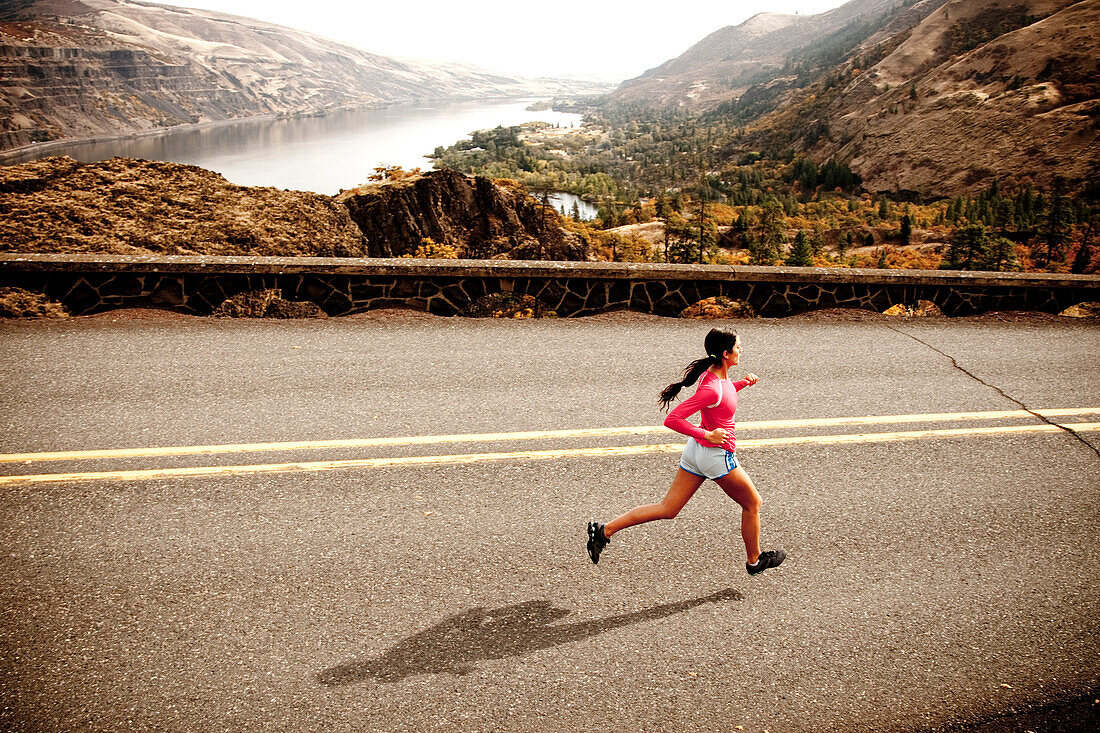 An athletic woman jogging along a deserted road on a beautiful fall day with the Columbia River Gorge in the distance Hood River, Oregon, USA