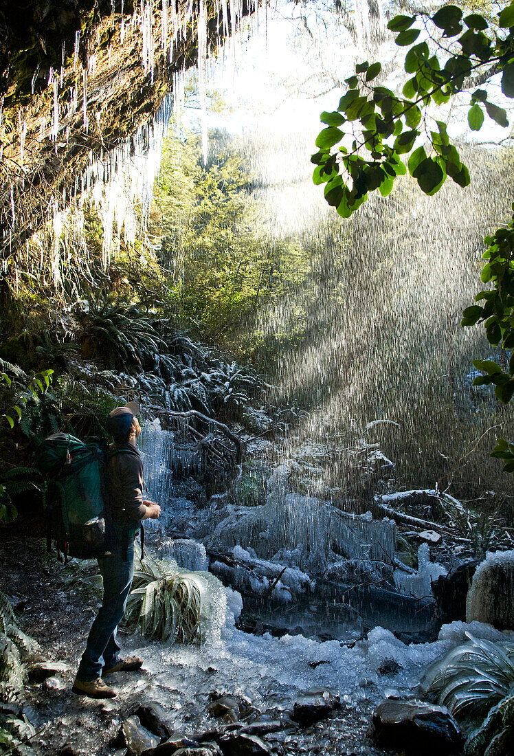 A young man looks up at the ice melt and sun rays, while hiking on an icy trail in Mt. Cook, New Zealand Mt. Cook, New Zealand