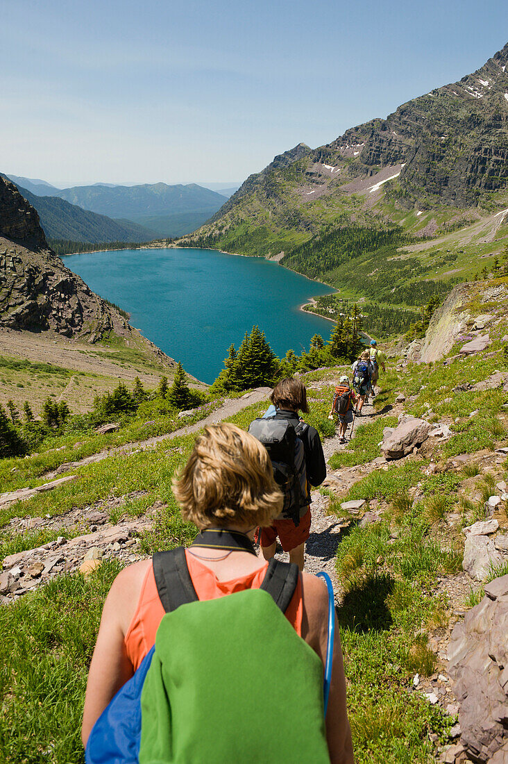 A group of backpackers hike down a trail towards an alpine lake, Glacier National Park, Montana Montana, USA