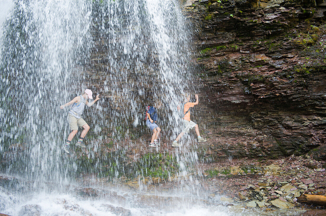 Three young girls explore behind a waterfall Alberta, Canada