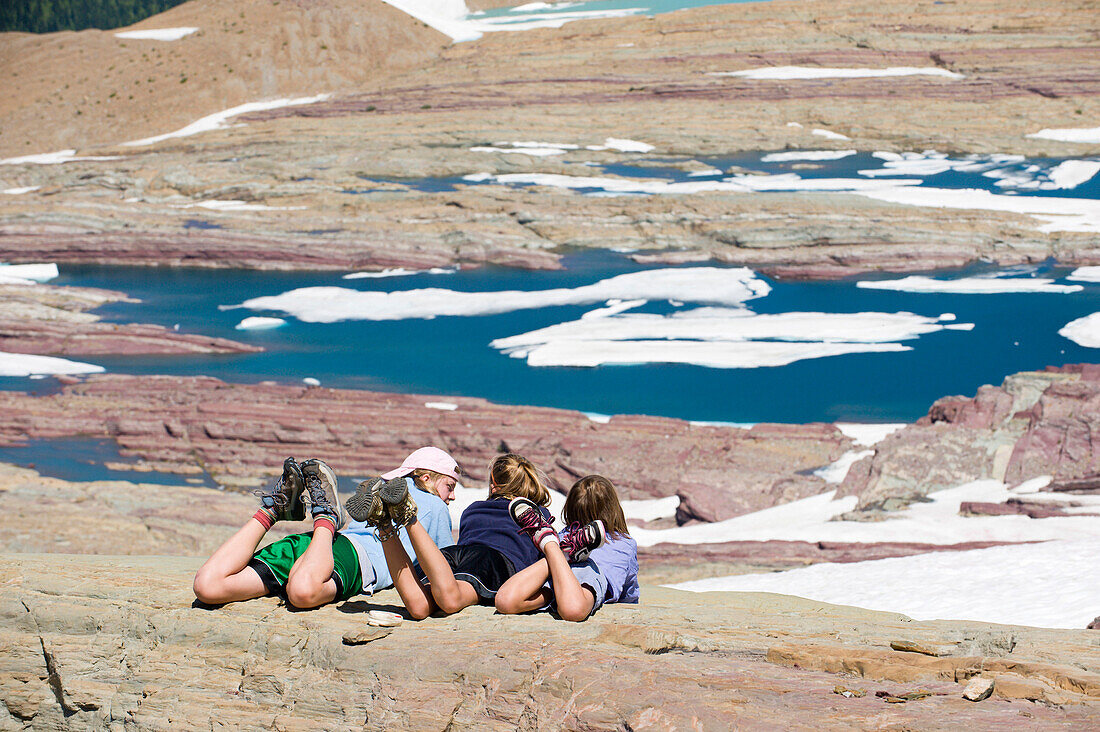 Three young girls relax and soak up the sunshine overlooking a glacier lake in Glacier National Park, Montana Montana, USA