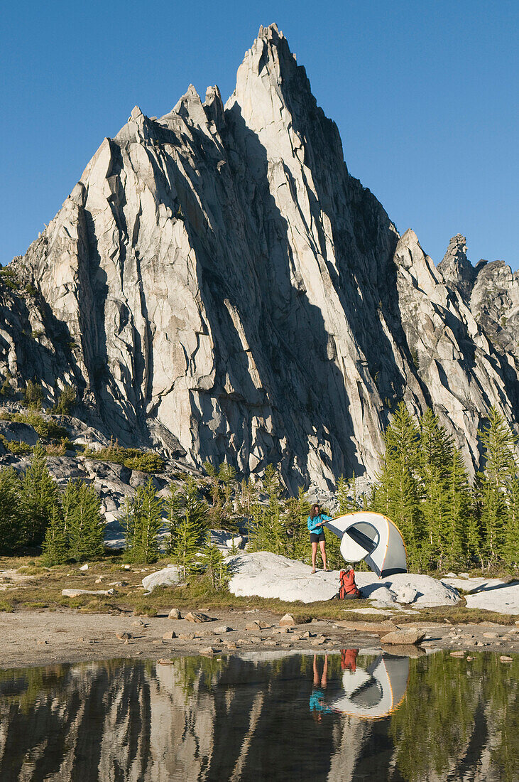 A woman camping on a pristine, alpine lake below a peak, Enchantment Peaks, Alpine Lakes Wilderness, Leavenworth, Washington Leavenworth, Washington, USA