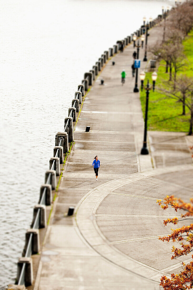 An athletic female in a blue jacket jogging near the Portland, Oregon waterfront Portland, Oregon, USA