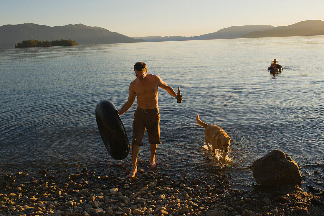 A young man and his dog come ashore after a swim in a lake Sandpoint, Idaho, USA