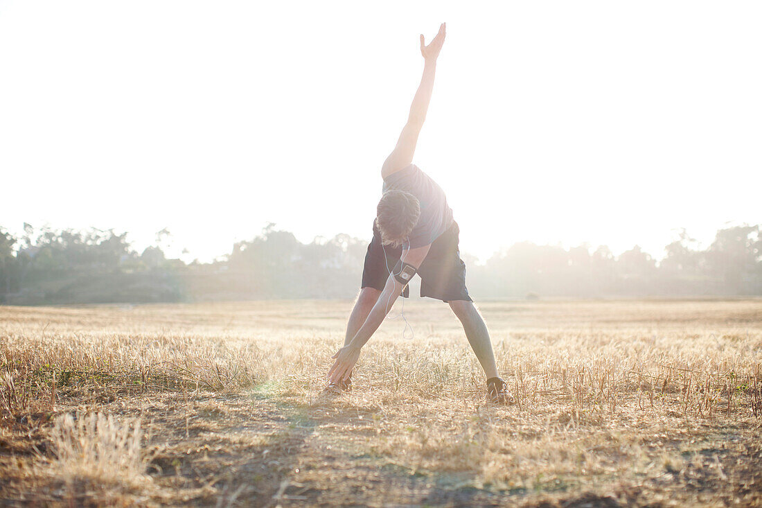 Man in his late 20's stretching before running it an open field in San Diego, California San Diego, California, USA