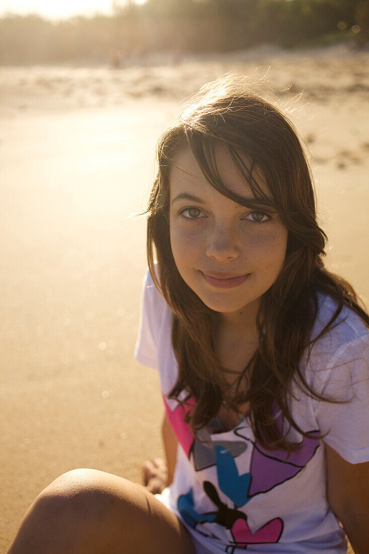A pre-teen girl looks up at the camera and smiles at Paia Beach, Maui, Hawaii as the sun rises Maui, Hawaii, USA