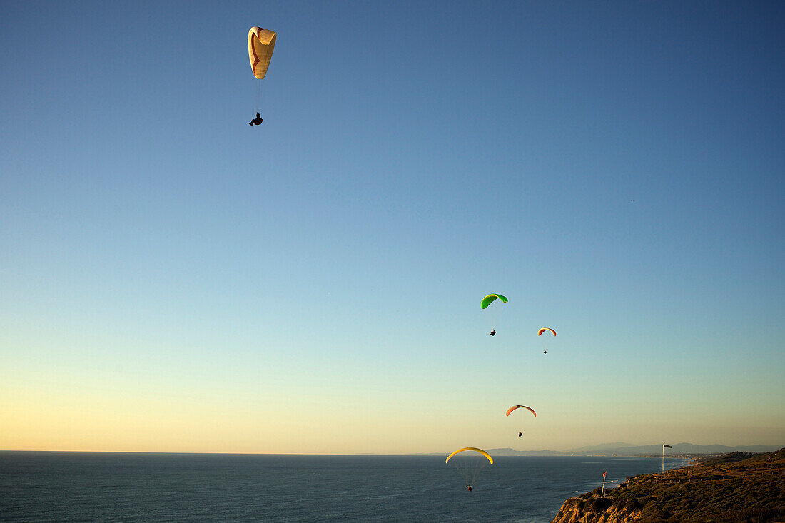 Five paragliders ride the wind at sunset over the ocean in California San Diego, California, USA