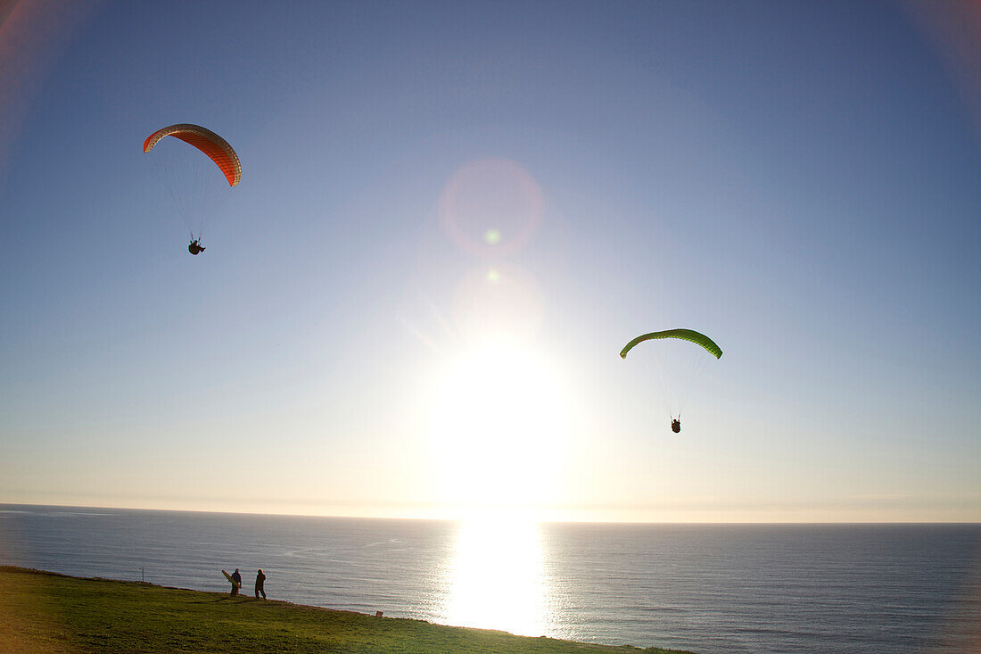 Two paragliders ride the wind at sunset over the ocean in California San Diego, California, USA