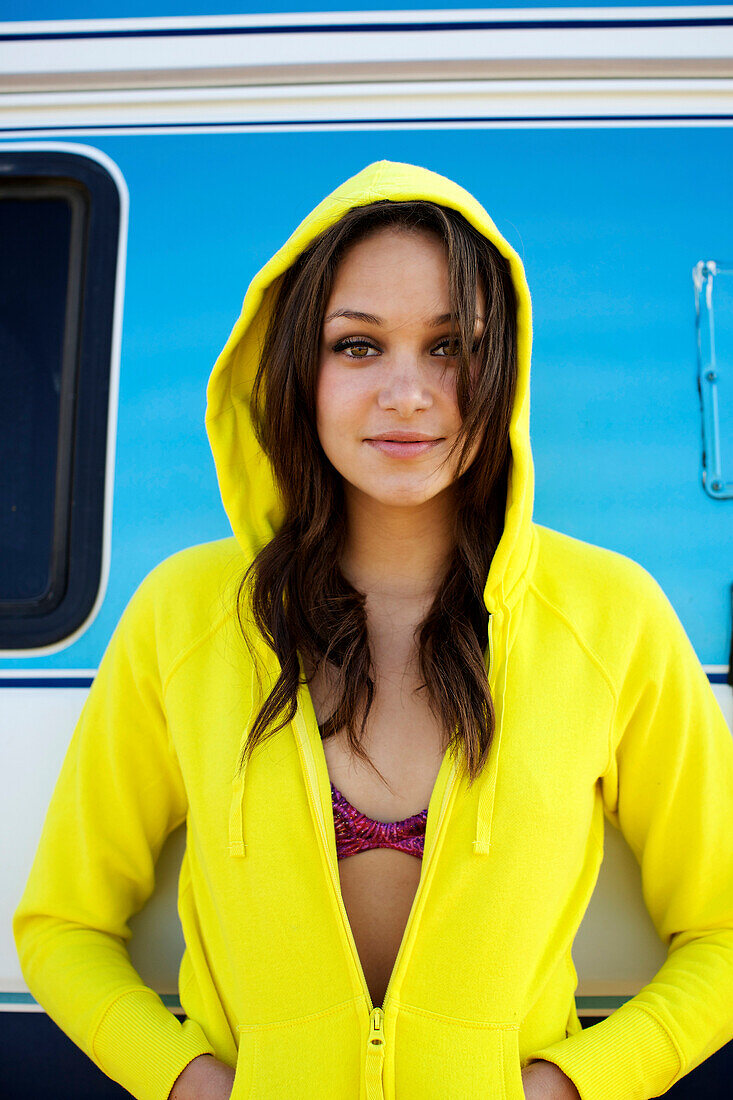 Female in her early 20's wearing a bright yellow hoodie poses in front of a vintage blue van San Diego, California, USA