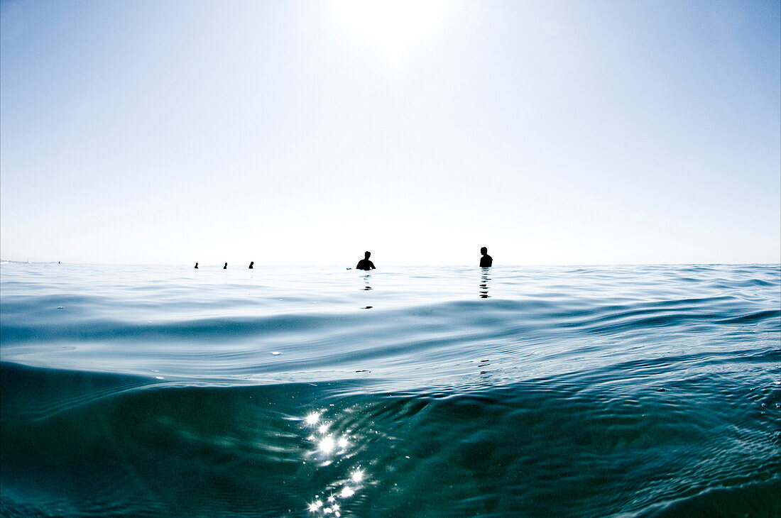 Water angle view of floating surfers waiting to catch waves on bright blue sky day Oceanside, California, USA