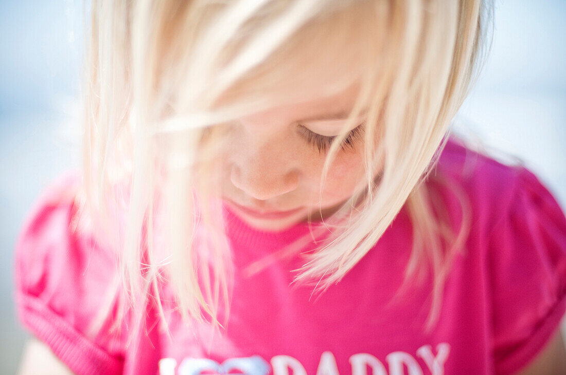 Select focus of a cute young blonde girl looking down at her pink shirt Oceanside, California, USA
