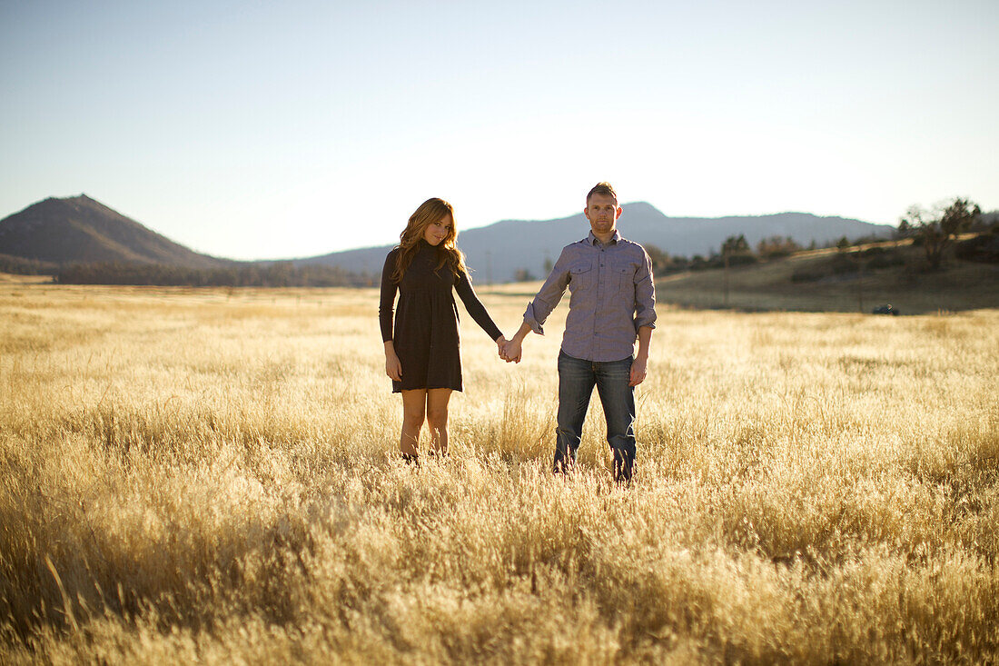 Couple hold hands, look as the camera and smile in an open field, San Diego, California, USA