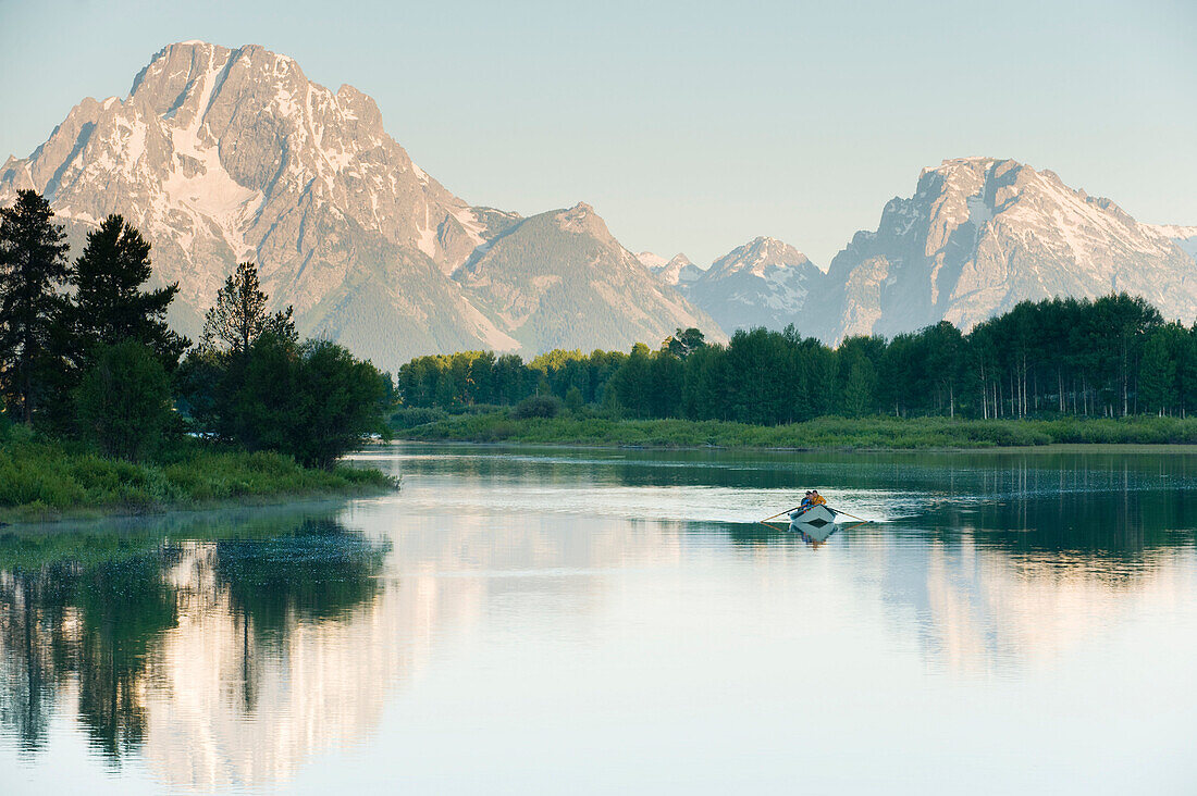 A lone drift boat floats in the reflected waters of a river Wyoming, USA