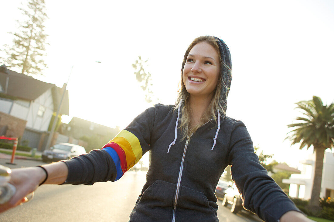 Young woman wearing a hoodie rides a cruiser bike Coronado, California, USA