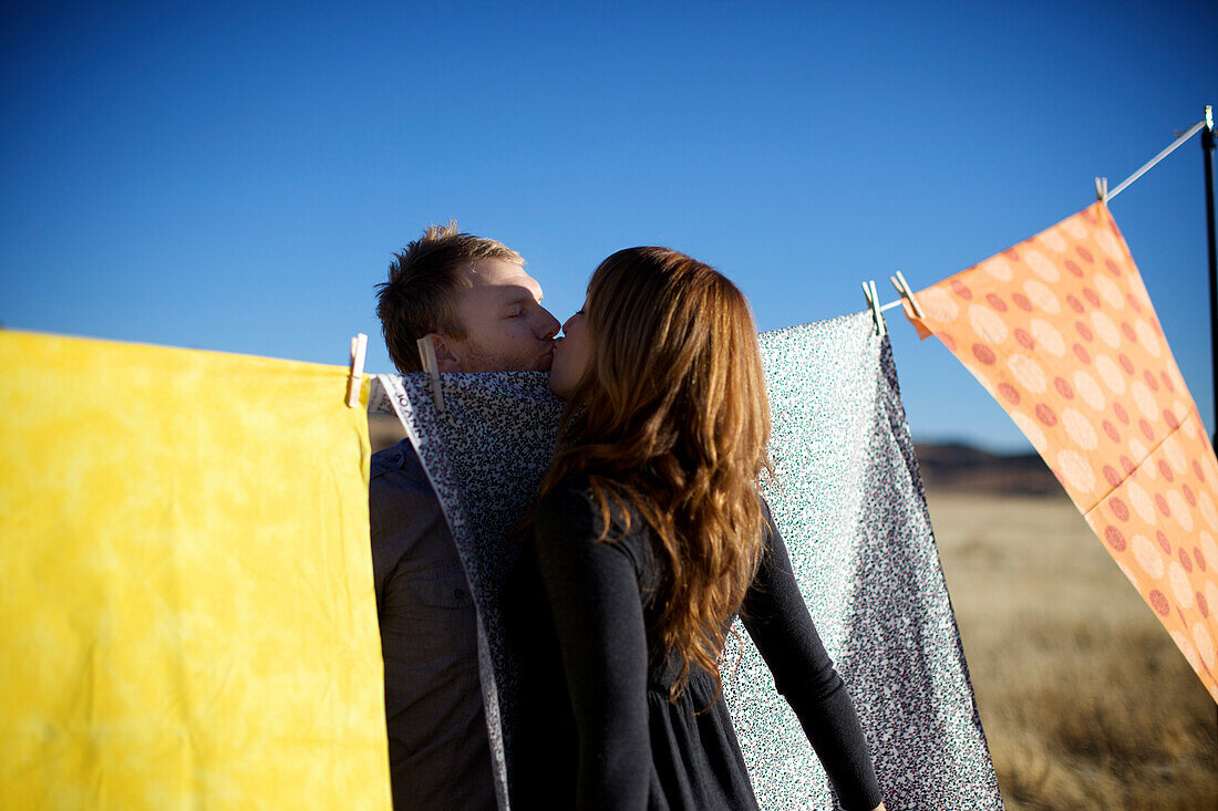 Couple kiss near colorful fabrics hung on a clothes line San Diego, California, USA