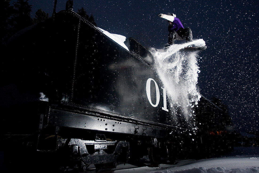 A male young adult jumps off a train at night in Colorado Breckenridge, Colorado, USA
