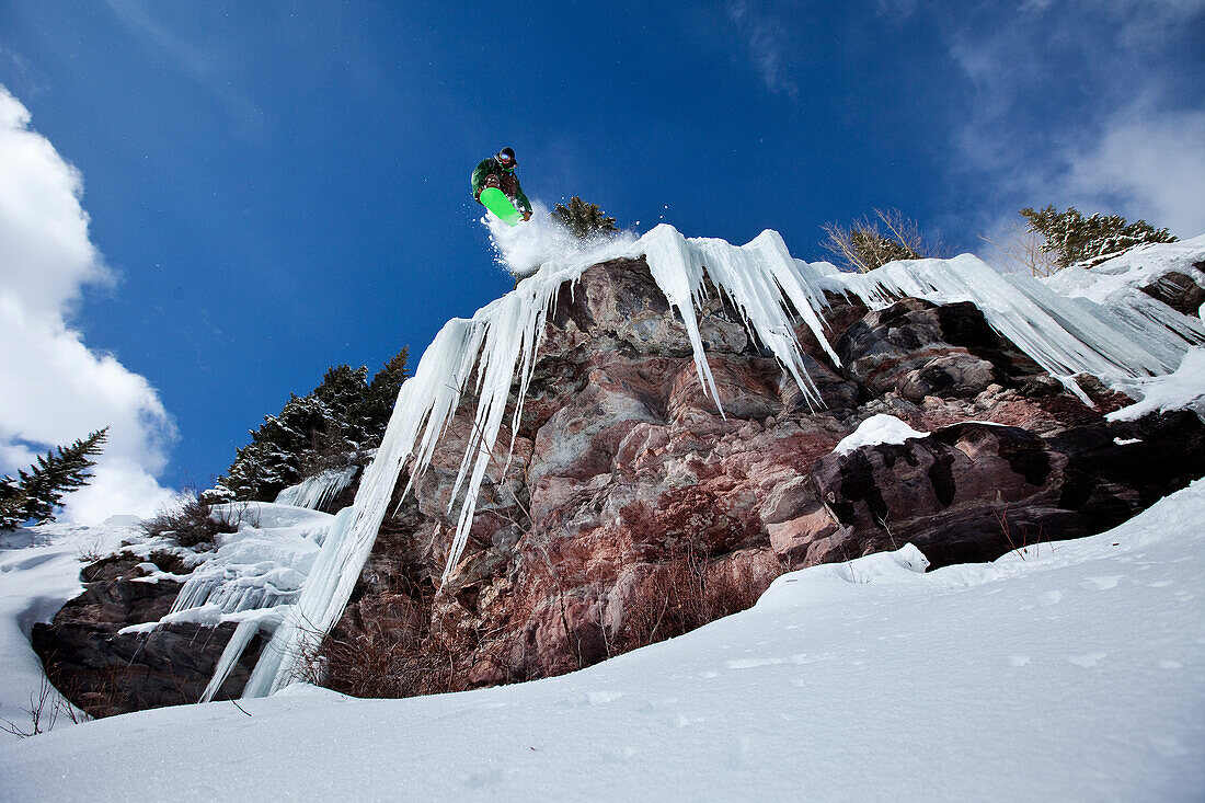 A male snowboarder jumps off an ice waterfall cliff on a sunny day in Colorado Vail, Colorado, USA