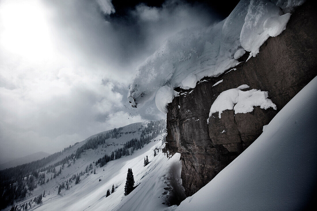 A snowboarder does a half cab off a cliff on a stormy powder day in Colorado Vail, Colorado, USA