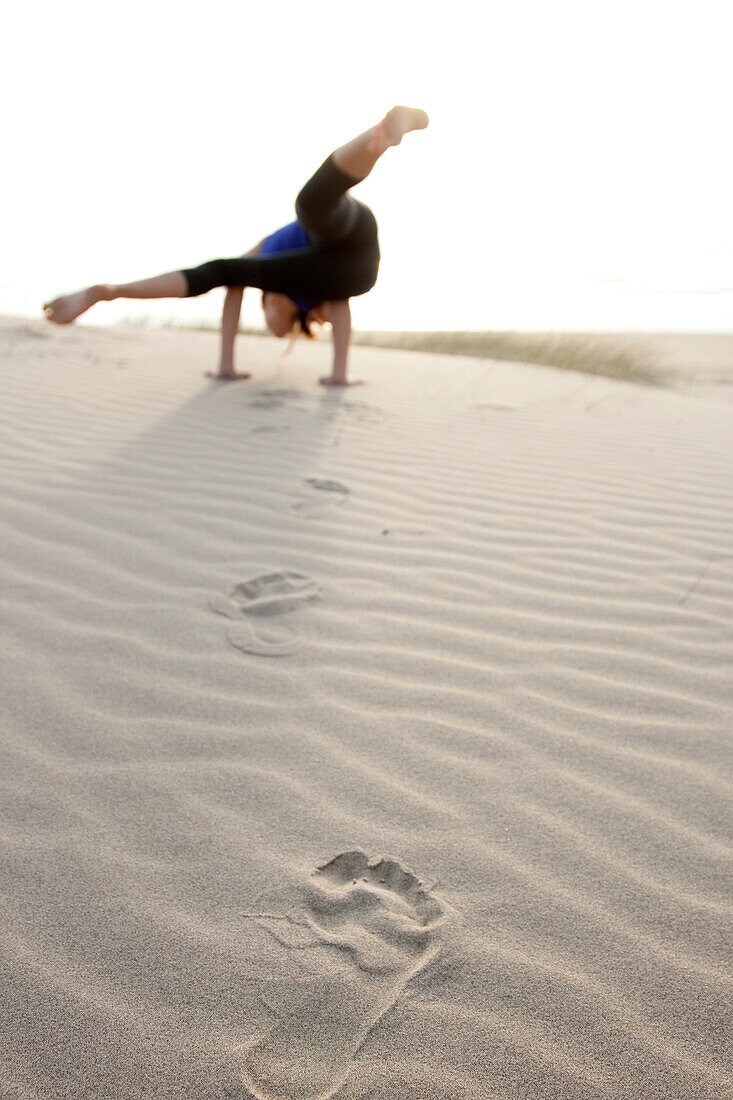 A woman doing yoga, leaves footprints while walking through the sand Cannon Beach, Oregon, USA