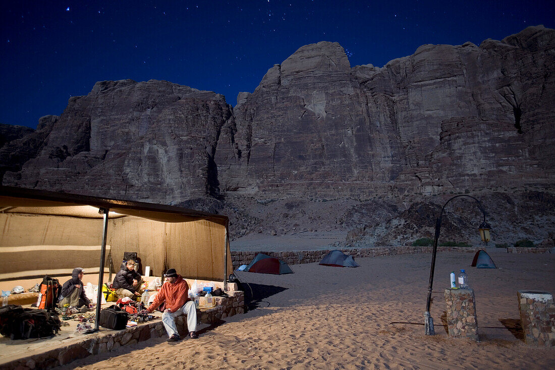 Three climbers organize gear in tent under starry sky Wadi Rum Village, Jordan