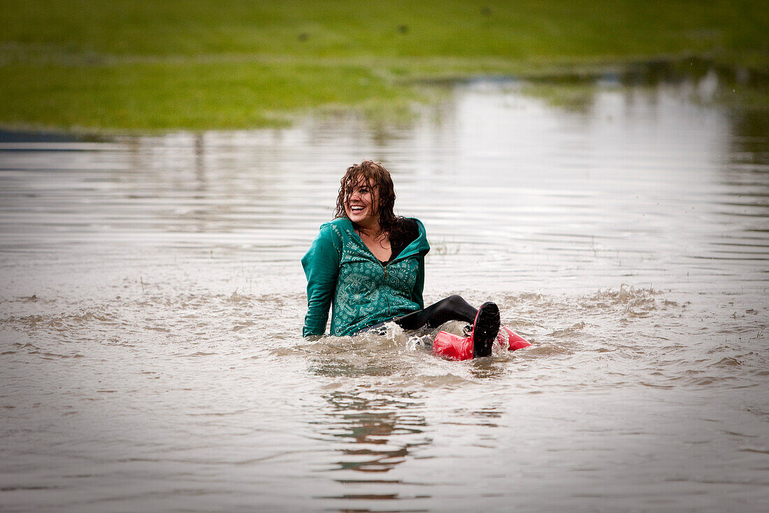 A young women laughs while sitting in a large puddle Sandpoint, Idaho, USA