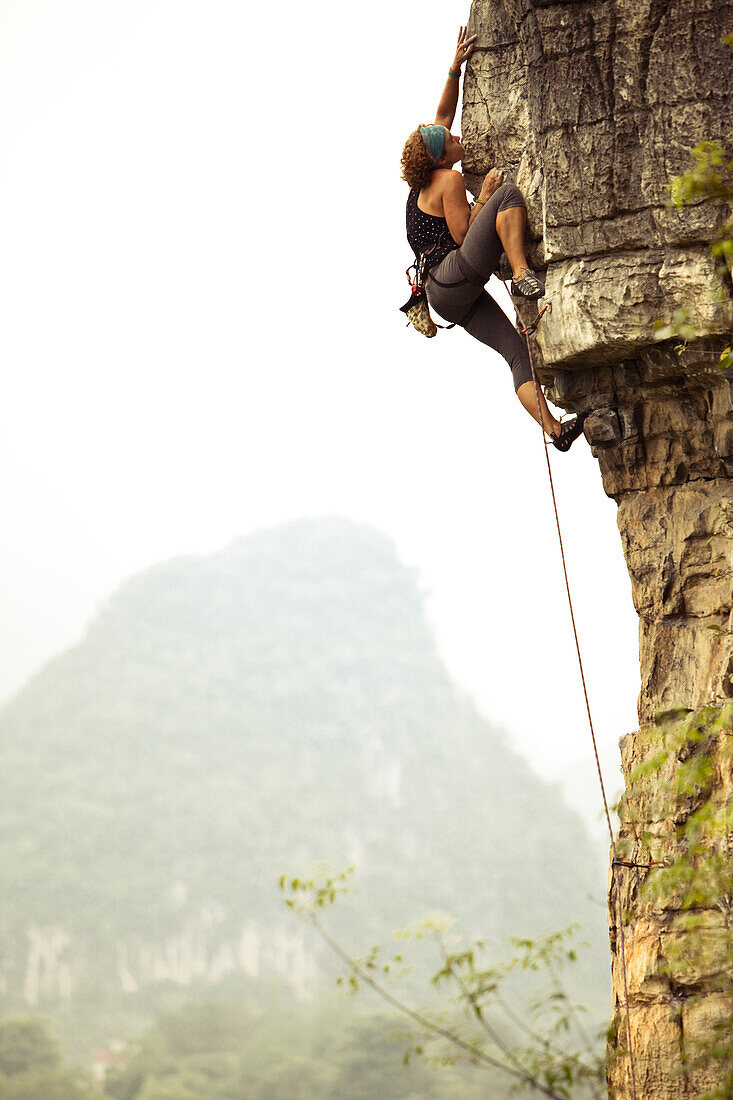 Female climber reaching out for a distant hold on overhanging limestone in China Yangshuo County, Guilin, Guangxi, China