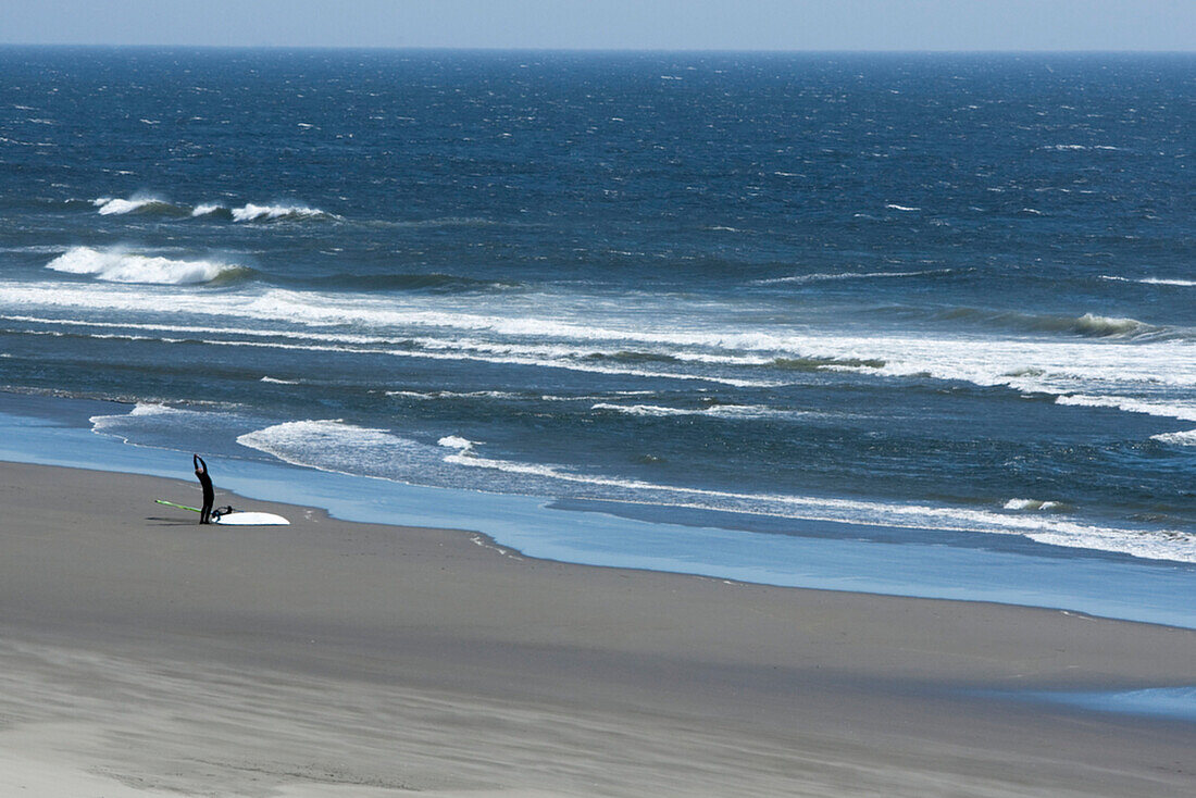 One man stretching on the beach with his windsurf board Astoria, Oregon, USA