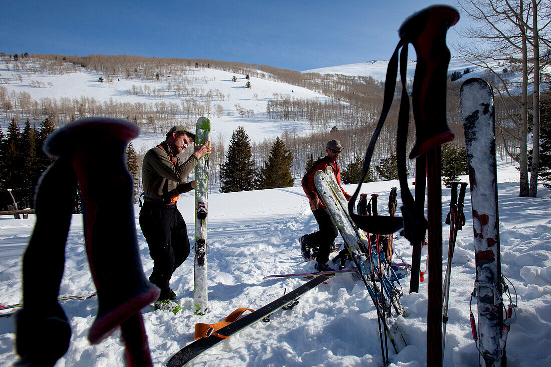Two men getting their skis ready in the snow and framed by ski poles Wendover, Nevada, USA