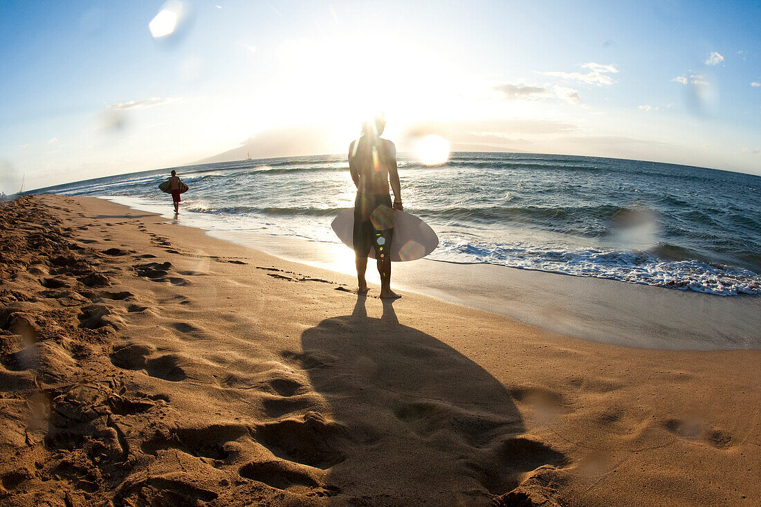 Two men walking on the beach with skimboards in search of the right spot in nice light Ka'anapali, Hawaii, USA