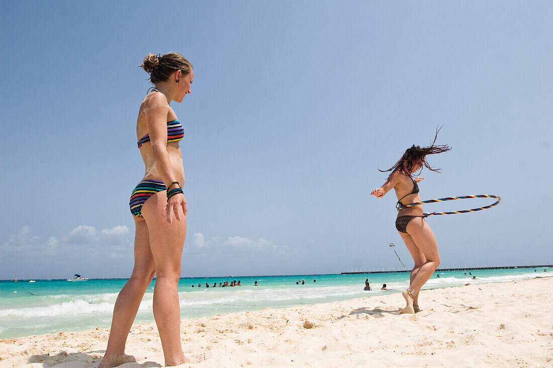 A girl watches as her friend is hula hooping on the beach in Mexico Playa Del Carmen, Quintana Roo, Mexico