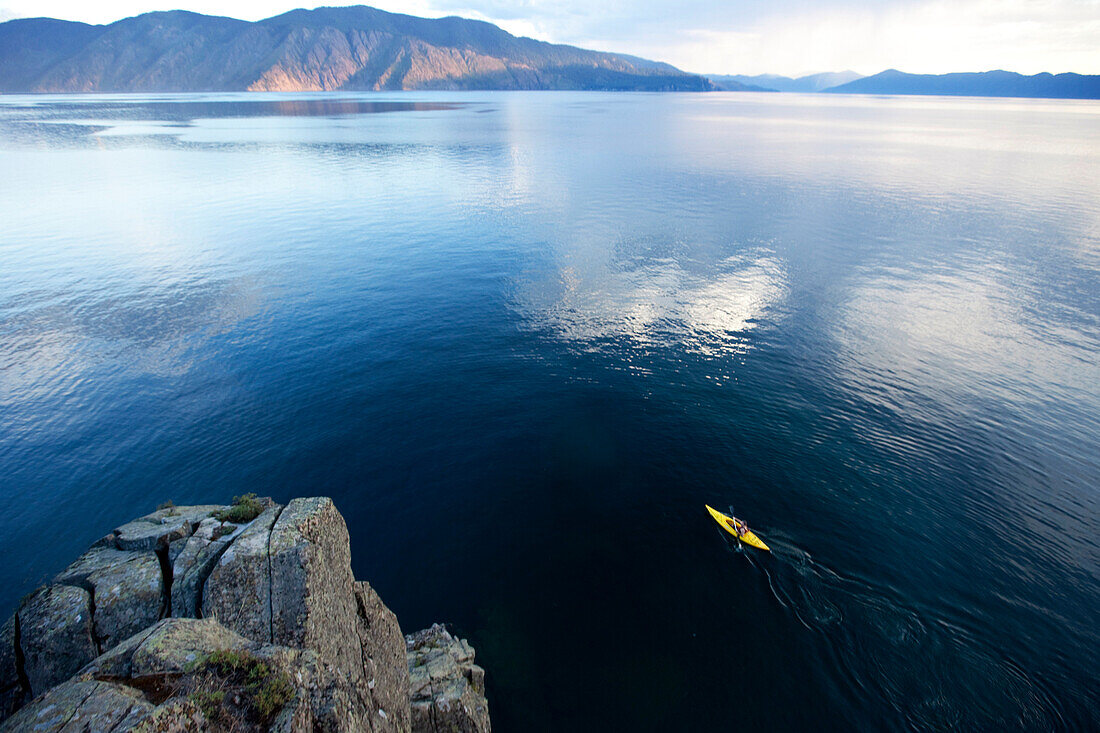 Young man paddles yellow kayak on lake Sandpoint, Idaho, USA