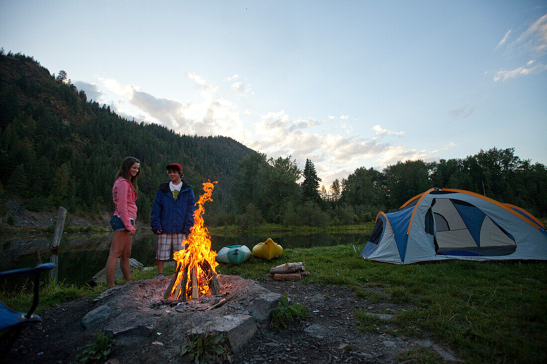 Young adult couple camping with a camp fire and kayaks on a beautiful summer evening Sandpoint, Idaho, USA