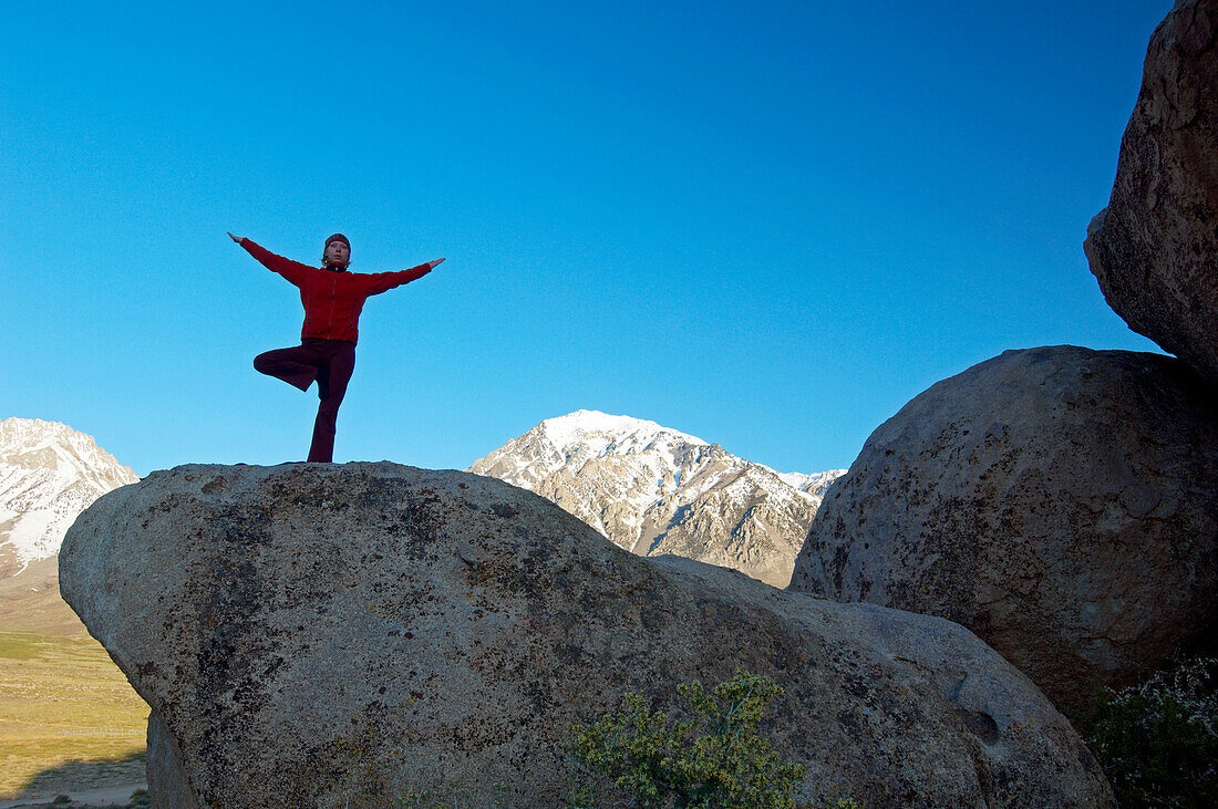 A woman practices yoga on top of a boulder Buttermilks, California, USA