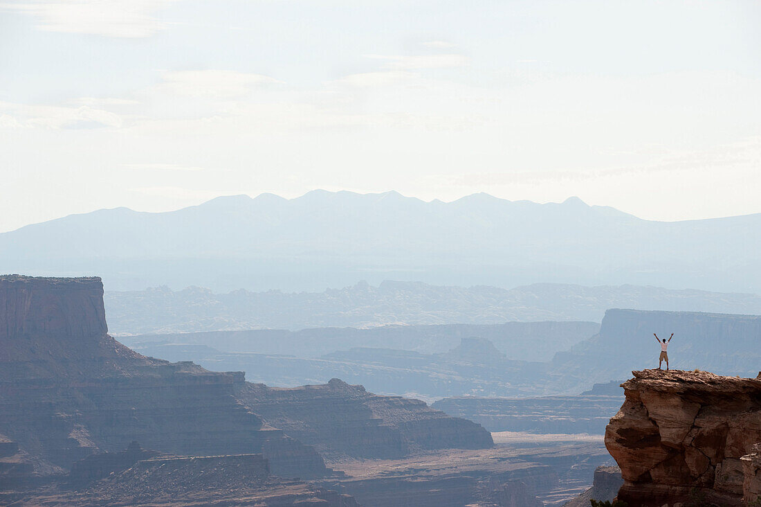 A young man enjoys the view from a rock on the edge of a canyon in Canyonlands National Park, UT, Moab, Utah, USA
