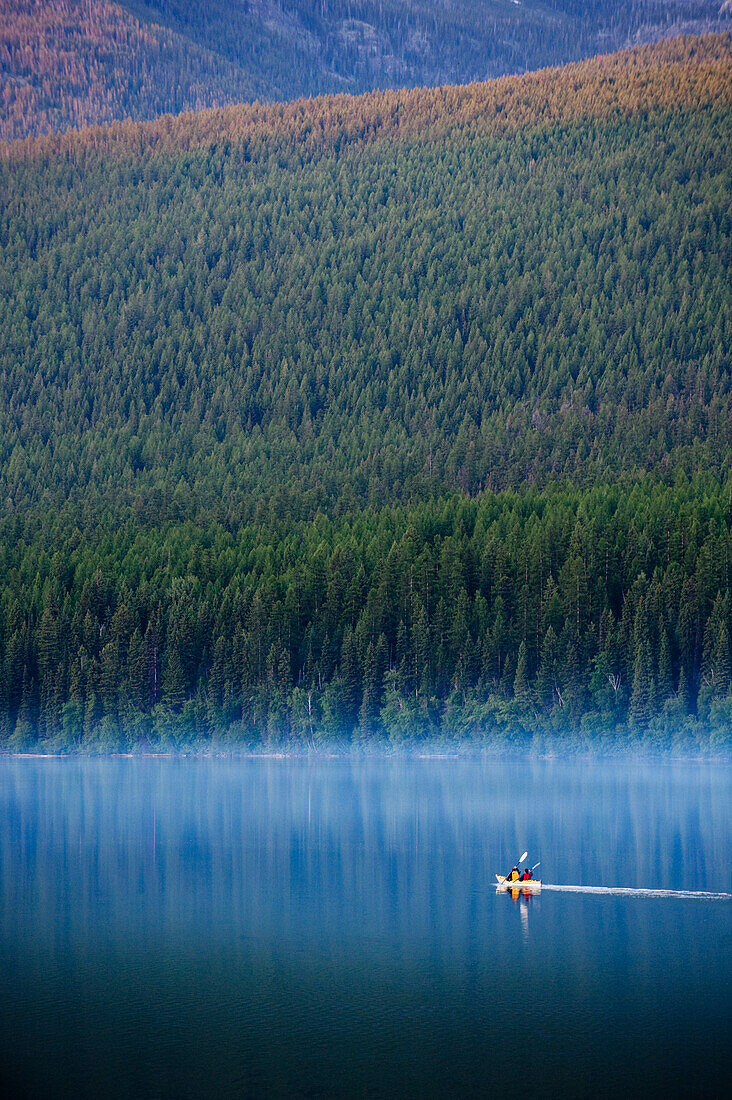 A couple paddles a kayak through a lake in Glacier National Park, MT Montana, USA