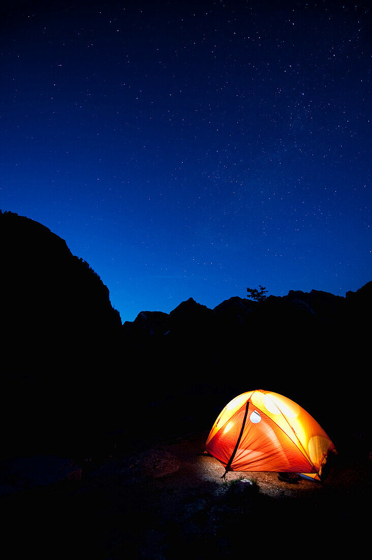 A tent glows by headlamp under a starry sky in Teton National Park, WY Wyoming, USA